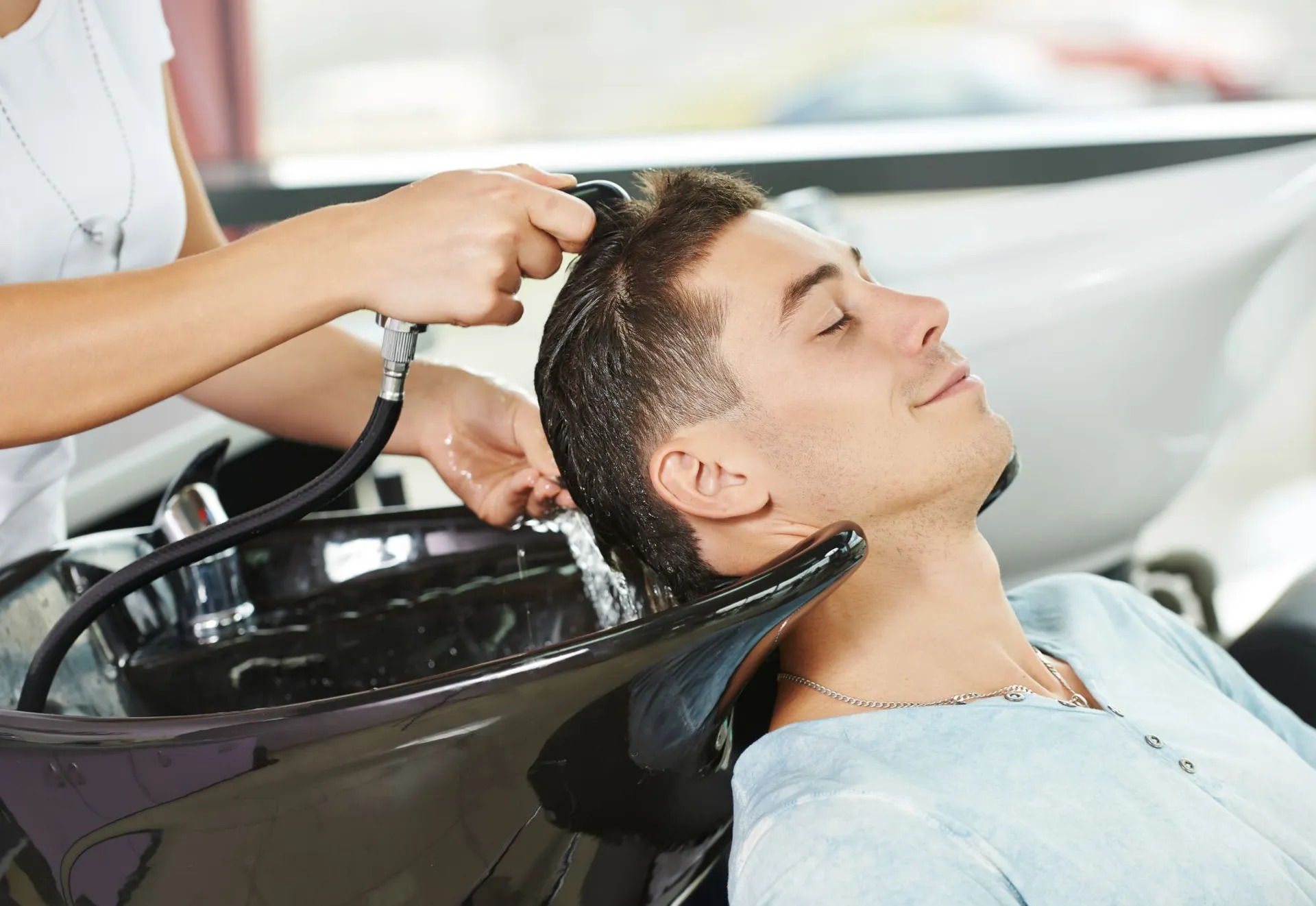 Stylist rinsing a client's hair at the salon shampoo bowl